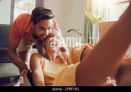 Lustiges Paar, das zusammen in das erste Haus zieht, Spaß hat und seine Freiheit genießt. Junge Vermählte genießen ihr neues Zuhause, machen Spaß und sind aufgeregt. Fröhliche Hausbesitzer, die beim Auspacken spielen Stockfoto