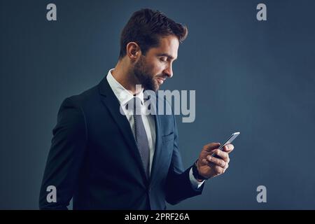 HES hat mehrere Verbindungen. Studioaufnahme eines hübschen jungen Geschäftsmannes mit einem Handy vor dunklem Hintergrund. Stockfoto