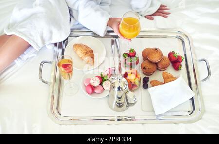 Das nenne ich Frühstück. Die Aufnahme einer unkenntlichen Frau, die auf ihrem Hotelbett ein gesundes Frühstück genießt, ist aus einem hohen Winkel zu sehen. Stockfoto