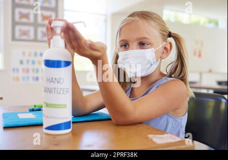 Kleine Schülerin desinfizierende Hand zum Schutz vor Flecken, Tragen einer Maske und Befolgen neuer Hygiene-Sicherheitsroutine. Kindergarten- oder Vorschulerinnen schützen sich vor Corona-Virus-Grippe Stockfoto