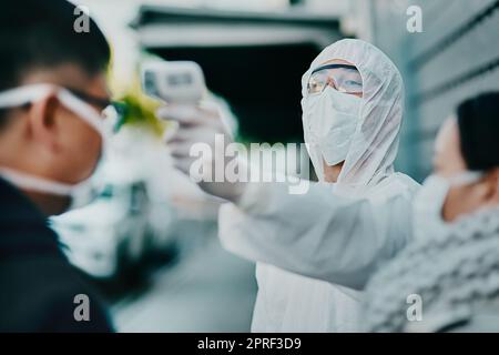 Reisebeschränkungen, Flughafen- oder Grenzmessung der Patiententemperatur im Freien mit einem Thermometer. Medizinischer Sicherheitsbeauftragter, der einen Mann am Eingang überprüft, um die Ausbreitung des Virus zu verhindern. Stockfoto