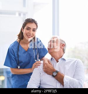 Wir kümmern uns wirklich um unsere Patienten. Porträt einer fröhlichen jungen Ärztin, die die Hand der Patienten hält, während sie in einer Klinik auf die Kamera blickt. Stockfoto