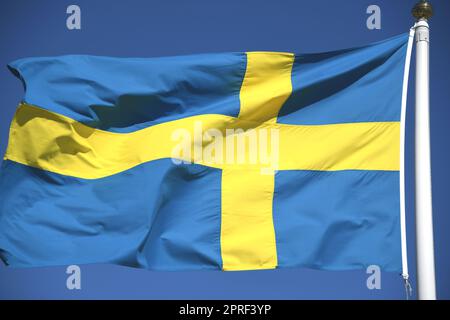 Die Nationalflagge Schwedens in den Farben Blau und Gelb im Wind auf einer Fahnenstange. Die Krone ist die Währung Schwedens. Stockfoto