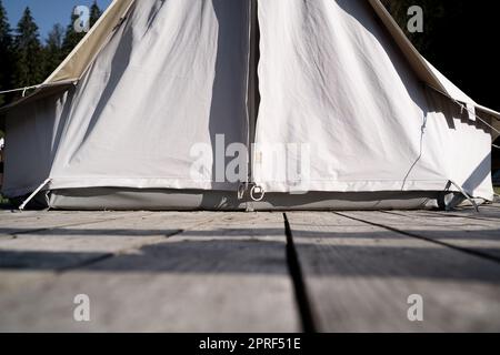 Nahaufnahme eines glitzernden Zelts mit weißem Stoffeingang auf einer Holzterrasse auf einer grünen Wiese, umgeben von Tannenbäumen Stockfoto