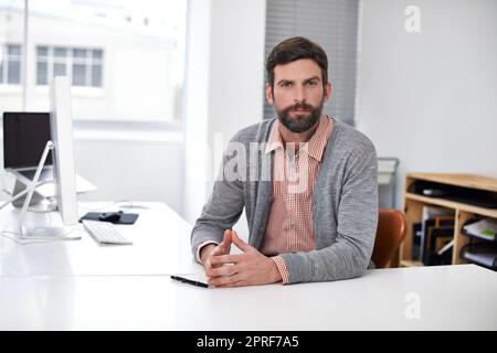 Nimm deine Konstruktionsbedürfnisse zur Hölle ernst. Porträt eines gutaussehenden jungen Mannes, der an einem Schreibtisch in einem Büro sitzt Stockfoto