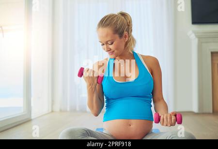 In Form zu bleiben ist auch für das Baby toll. Eine Schwangerin arbeitet zu Hause mit Gewichten. Stockfoto