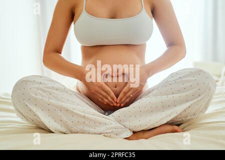 Liebe macht das Leben schön. Eine Schwangerin hält ihren Bauch mit ihren Händen, die eine Herzform bilden. Stockfoto