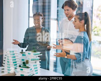 Ein Team von Architekten, Designern oder Ingenieuren, die eine Gebäudekonstruktion oder einen Prototyp in einer Besprechung planen und besprechen. Eine Gruppe von Stadtplanern führt eine Diskussion im Sitzungssaal und ist mit dem Modell zufrieden Stockfoto