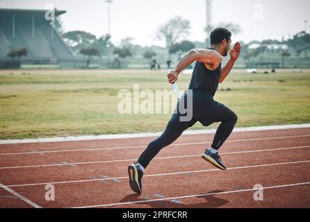 Das Relais zum Laufen bringen. Aufnahme eines gutaussehenden jungen Athleten, der während eines Staffelrennen mit einem Schlagstock läuft Stockfoto