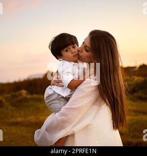 Mutter und Sohn, eine Bindung, die nie gebrochen werden kann. Eine junge Mutter küsst ihren Sohn auf der Wange im Freien. Stockfoto