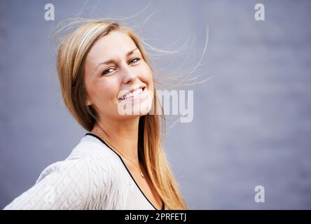 Mädchencharme von nebenan. Porträt einer schönen jungen Frau, die sich draußen vor grauem Hintergrund posiert Stockfoto