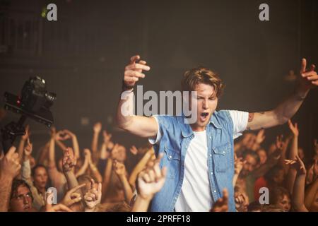 Auf einer Welle von Fans. Ein aufgeregter junger Mann jubelt auf den Schultern eines Freundes, während seine Lieblingsband spielt Stockfoto