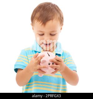 Es fühlt sich so voll an. Studiofoto eines kleinen Jungen, der auf ein weißes Sparschwein schaut Stockfoto