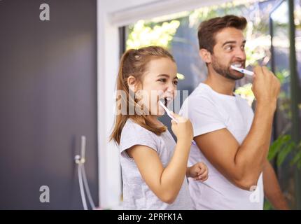 So putzen wir unsere Zähne. Ein hübscher Vater und seine Tochter putzen sich ihre Zähne im Badezimmer zu Hause. Stockfoto