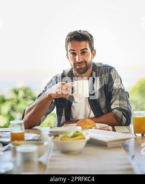 Ich kann den Tag nicht ohne eine starke Tasse Kaffee beginnen. Porträt eines hübschen jungen Mannes, der zu Hause frühstückt. Stockfoto