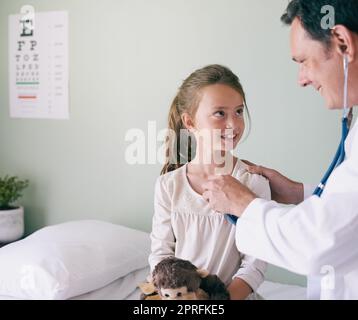 Der Besuch des Arztes ist keine Strafe. Ein männlicher Arzt überprüft die Herzfrequenz seiner jungen Patienten. Stockfoto