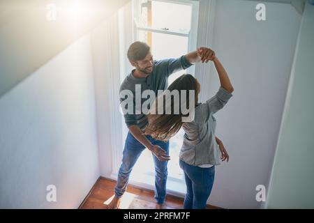 Tanzt bis die Sonne untergeht. Ein liebevolles junges Paar tanzt zu Hause fröhlich. Stockfoto