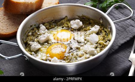 Grüne Shakshuka mit Spinat und Feta in einer Pfanne auf einem Tisch mit Brot Stockfoto