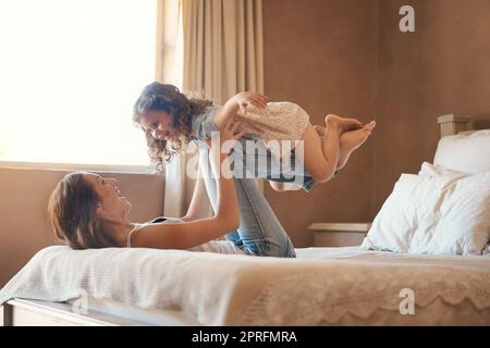 Eine Mutter und Tochter haben Spaß zu Hause, während die Mutter ihr Kind hochhebt und herumspielt. Stockfoto