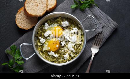 Grüne Shakshuka mit Spinat und Feta in einer Pfanne auf einem Tisch mit Brot Stockfoto