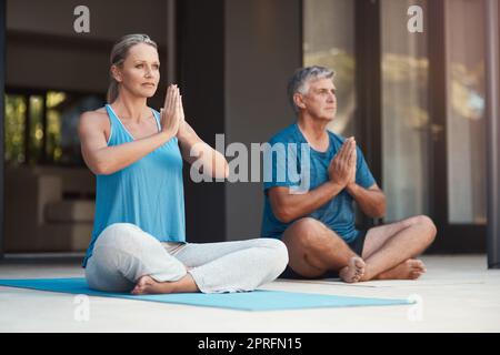 Lassen Sie allen Stress los und lassen Sie den Frieden über sich ziehen. Ein reifes Paar nimmt friedlich eine Yoga-Pose mit gekreuzten Beinen und zusammengesteppten Händen ein. Stockfoto