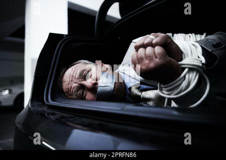Gefesselt und geknebelt. Ein ängstlicher Geschäftsmann, gefesselt und geknebelt im Kofferraum seines Autos Stockfoto
