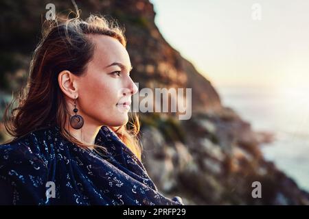 Verloren in Gedanken am Meer. Eine attraktive junge Frau genießt einige Zeit im Freien. Stockfoto