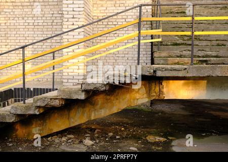 Alte Betontreppen mit gelbem Metallgeländer, die zum Gebäude führen. Stockfoto