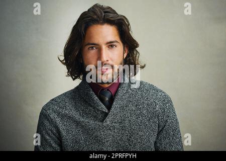 Hes hat seinen Blick auf dich gerichtet. Porträt eines stilvoll gekleideten Mannes, der vor grauem Hintergrund im Studio posiert. Stockfoto