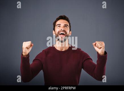 Es ist ein Wunder. Studioaufnahme eines hübschen jungen Mannes, der vor grauem Hintergrund jubelt. Stockfoto