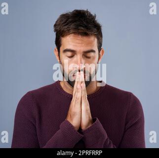 Lasst uns im Gebet den Kopf beugen...Studioaufnahme eines hübschen jungen Mannes, der vor grauem Hintergrund betet. Stockfoto