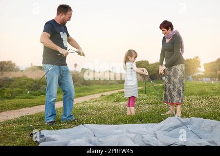 Viele Hände machen leichte Arbeit. Eine junge Familie, die zusammen ein Zelt aufstellt. Stockfoto