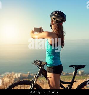 Mountainbiken ist eine Flucht. Eine junge Frau, die ein Bild von der schönen Landschaft beim Mountainbiken macht. Stockfoto