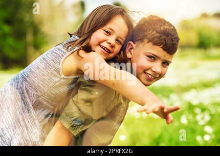 Liebe und Lachen teilen. Porträt eines entzückenden kleinen Jungen, der seiner kleinen Schwester eine Huckepack-Fahrt draußen gab. Stockfoto