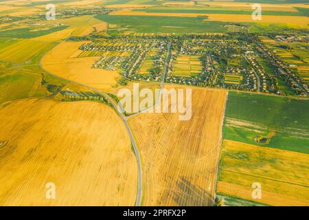 Blick Aus Der Vogelperspektive Auf Village Und Hay Rolls, Straw Field Landscape Am Sommerabend. Heuhaufen, Hay Roll bei Sonnenaufgang. Landschaftliche Landschaften in der Erntesaison. Stockfoto