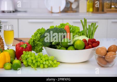 Frisches Gemüse, Obst und Eier auf einem weißen Tisch in der modernen Küche. Stockfoto