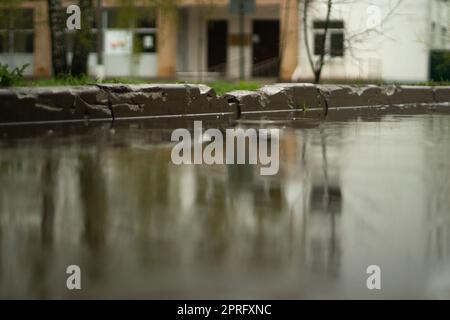 Regen draußen. Große Pfütze im Hof. Nasses Wetter. Oberfläche der Pfütze. Wasser auf der Straße. Stockfoto