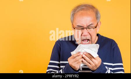 Asiatische ältere Mann Erkältung mit Grippe und Niesen von Krankheit Virus Problem verwenden Gewebe Studio Schuss isoliert auf gelbem Hintergrund, Portrait älterer alter Mann Stockfoto