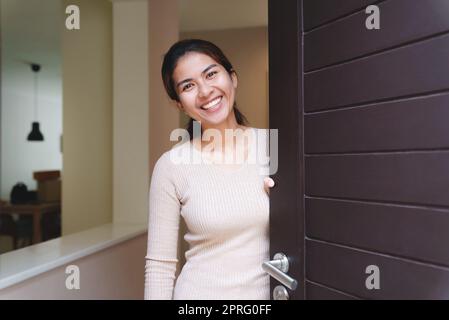 Lächelnde Frau, die die Tür öffnet, heißt das Haus willkommen Stockfoto