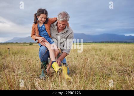 Viel Spaß mit der Familie auf dem Bauernhof, Großeltern und Mädchen haben Spaß in der Natur, bereiten Sie sich auf den gemeinsamen Spaziergang vor. Lächelndes Kind und liebevoller Großvater, der die Natur erkundet und einen Spaziergang auf dem Land oder auf dem Feld genießt Stockfoto