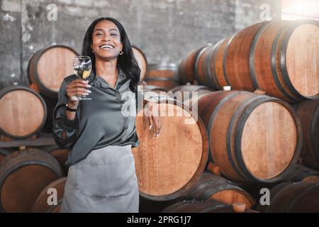 Porträt, Frau und Winzer mit einem Glas mit Holzfässern Weißwein in einem Weinkeller oder einer Destillerie. CEO oder Geschäftsinhaber, der für die Start-up-Produktion von Alkohol und Weingütern, Lagerhallen oder Fabriken arbeitet. Stockfoto