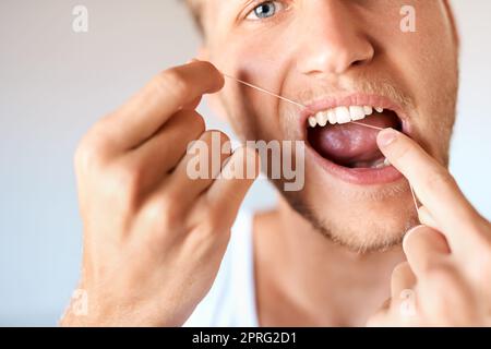 Keime und Plaque sind keine Chance. Nahaufnahme eines jungen Mannes, der zu Hause seine Zähne mit Zahnseide verputzt hat. Stockfoto