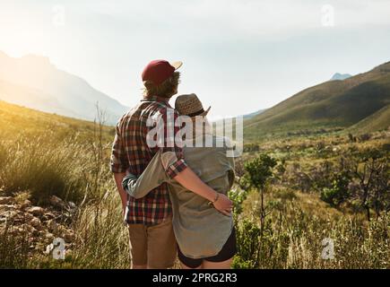 Erklimmen Sie einen Berg, um zum guten Leben zu gelangen. Rückansicht eines jungen Paares, das einen Bergblick in der Natur bewundert. Stockfoto