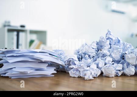 Papierkram häufen sich. Ein Haufen zusammengeknüllter Papierkram sitzt auf einem Schreibtisch. Stockfoto