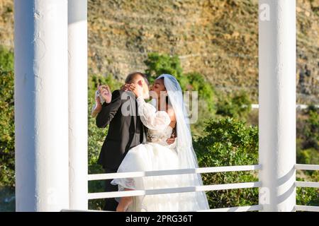 Junge, schöne, interracial Jungvermählte küssen sich im Pavillon vor dem Hintergrund der sonnigen Berge Stockfoto