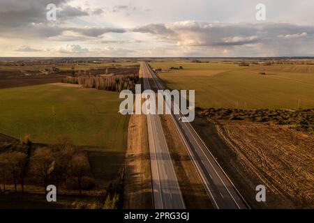 Drohnenaufnahmen von der Autobahn, umgeben von Landwirtschaftsfeldern und Wäldern am Frühlingsabend Stockfoto