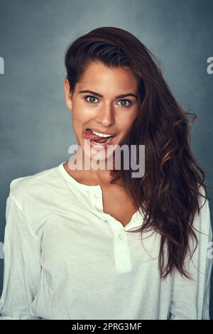 Lass dein Haar runter. Porträt einer schönen jungen Frau, die im Studio ein lustiges Gesicht vor einem grauen Hintergrund zieht. Stockfoto