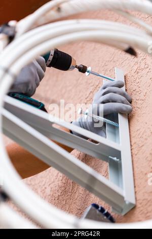 Nahaufnahme eines männlichen Arbeiters, der eine Wandhalterung für eine Außenklimaanlage installiert. Stockfoto