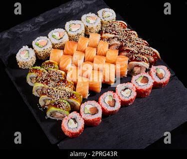 Japanisches Sushi-Set. Verschiedene Arten von Brötchen auf einem Steinbrett für Sushi auf schwarzem Hintergrund. Stockfoto