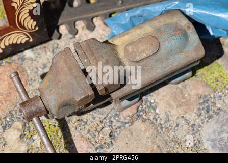 Ein alter Schraubstock steht auf einem gepflasterten Boden. Stockfoto